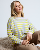Woman wearing a striped sweater sitting on a textured surface with a light background