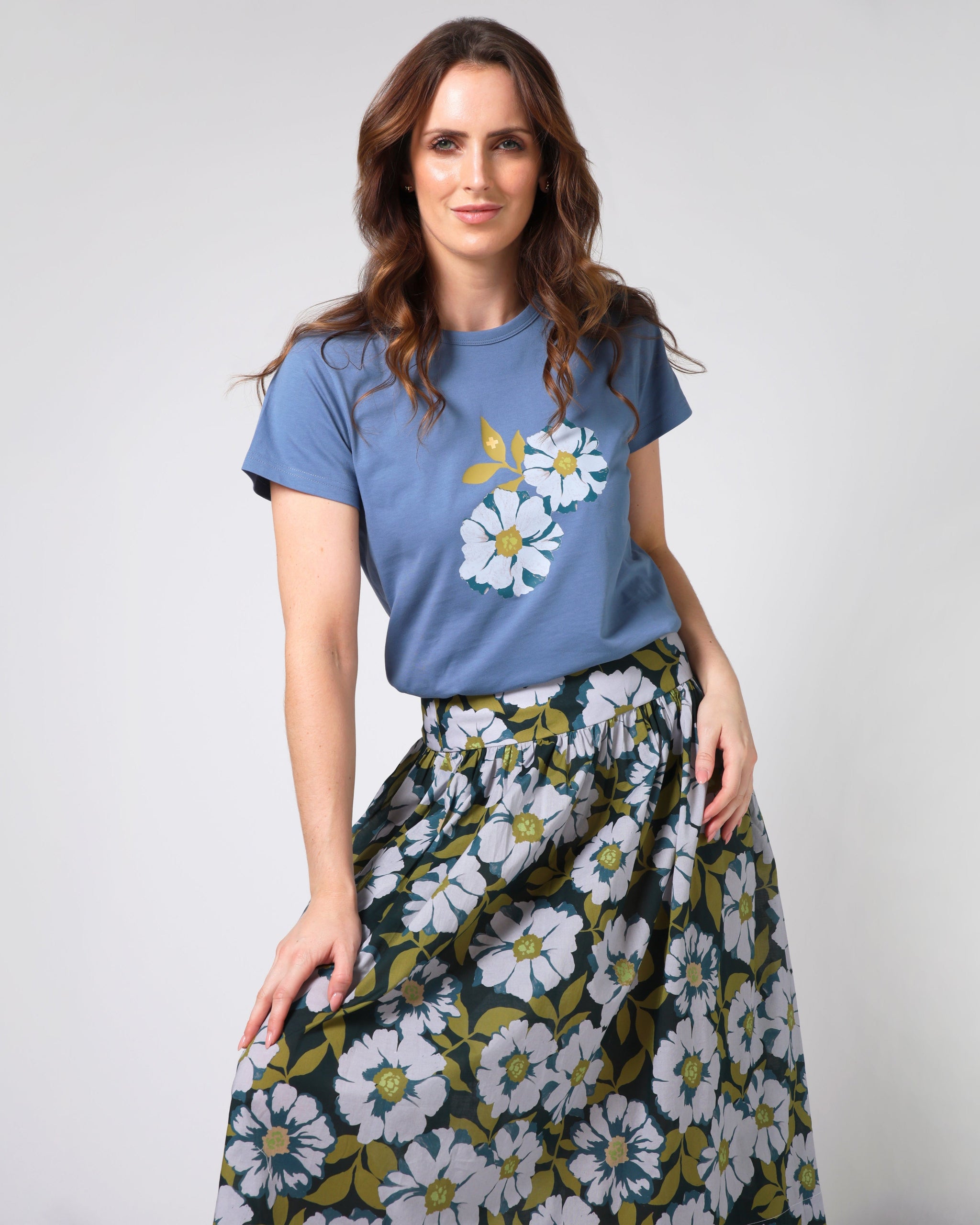 Woman wearing a blue t-shirt with floral design and a floral skirt on a plain background
