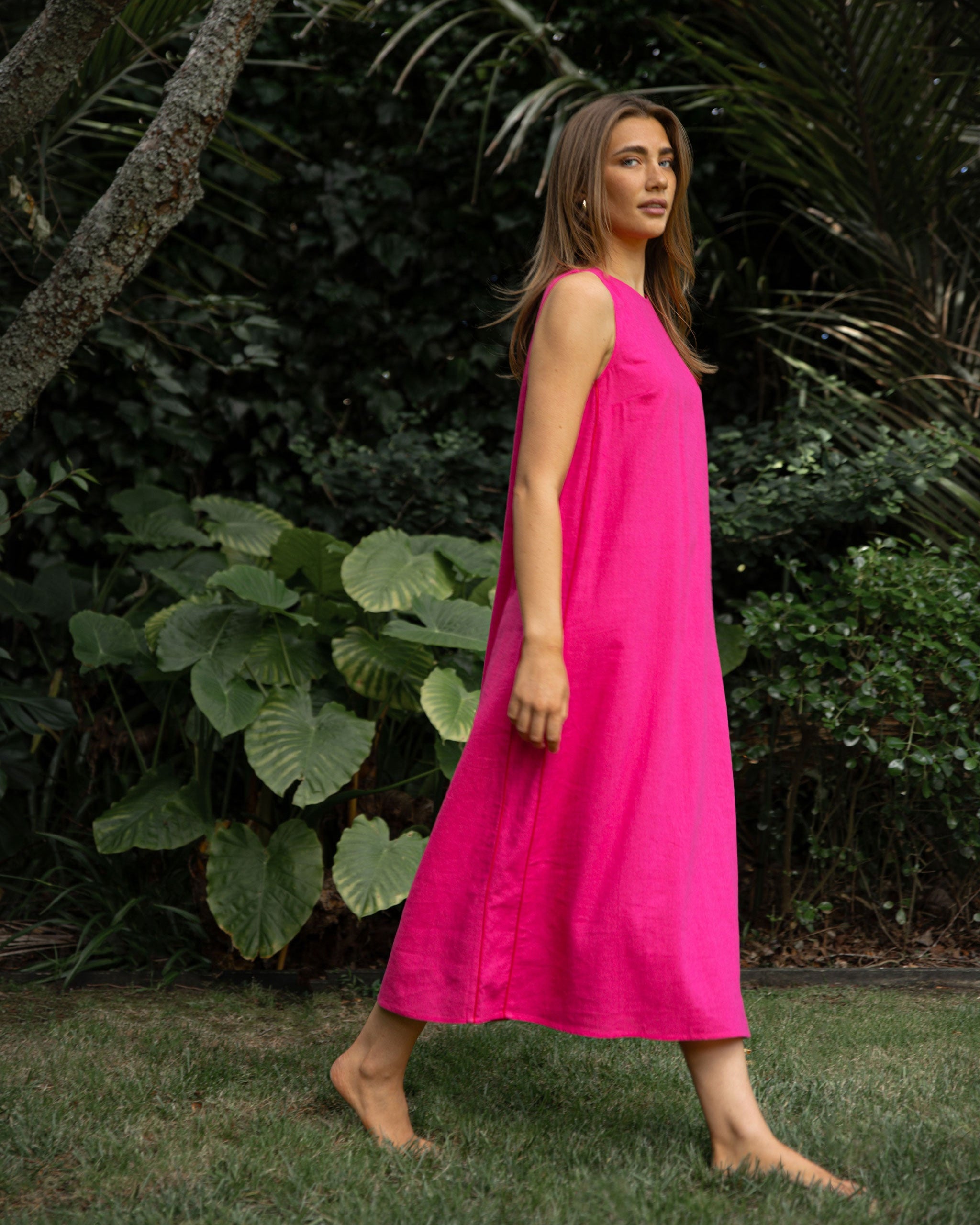Woman in a bright pink dress standing in a garden with green foliage.