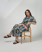Woman sitting on a chair wearing a floral dress against a plain background