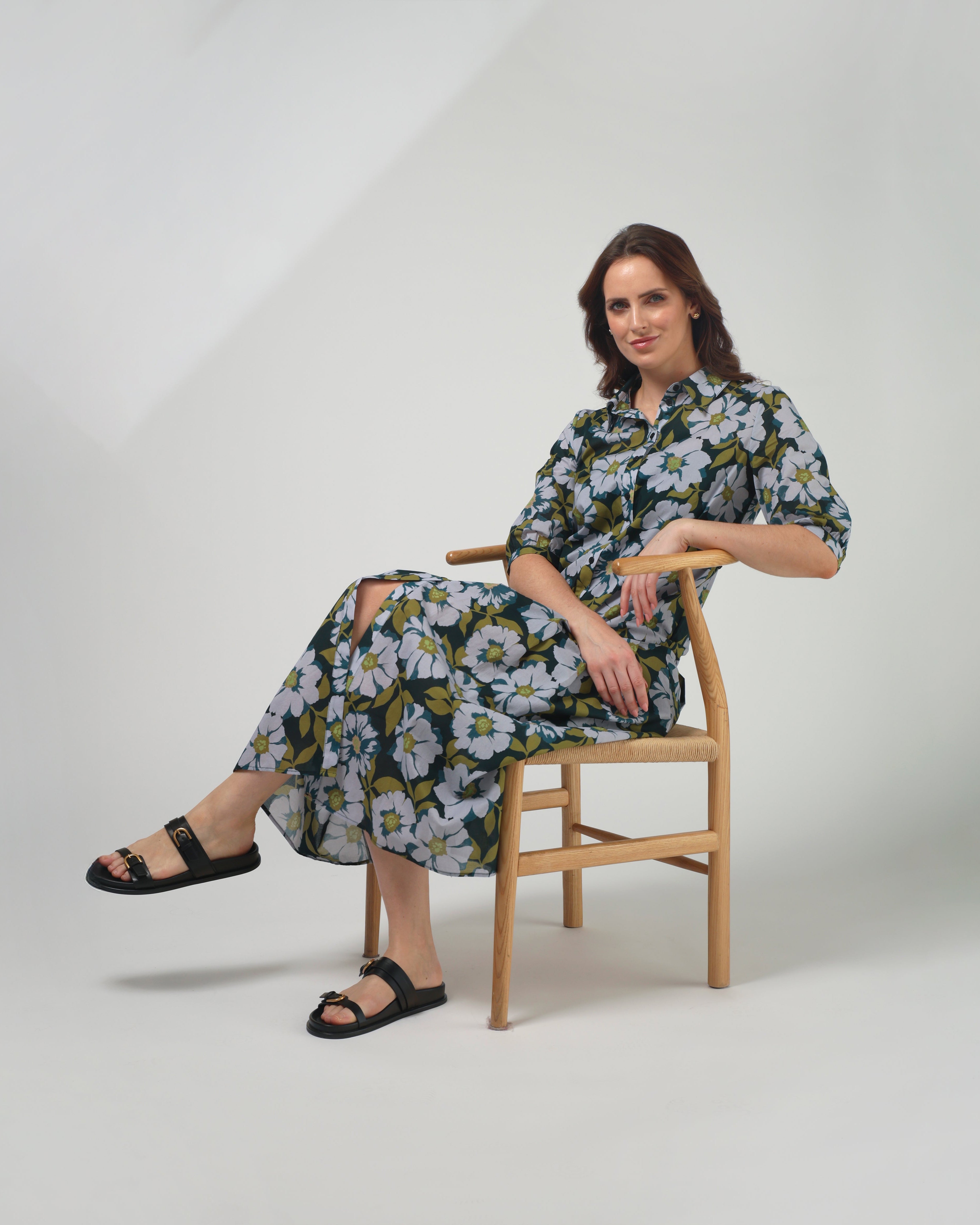 Woman sitting on a chair wearing a floral dress against a plain background